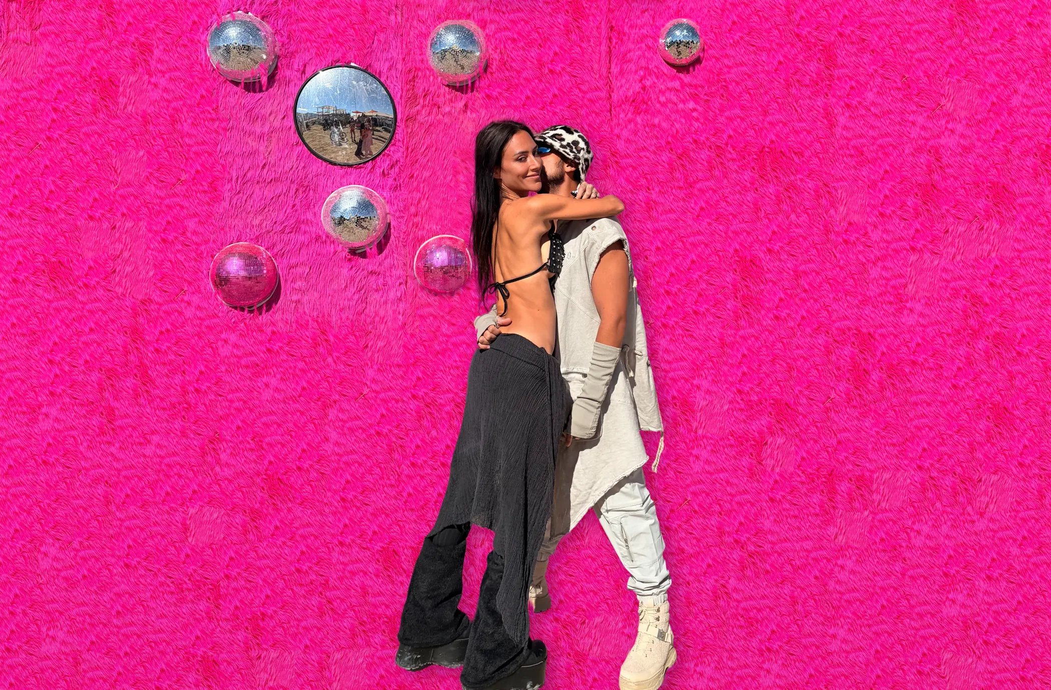 Léa and Damien embracing in front of a pink fur wall dotted with mirrors